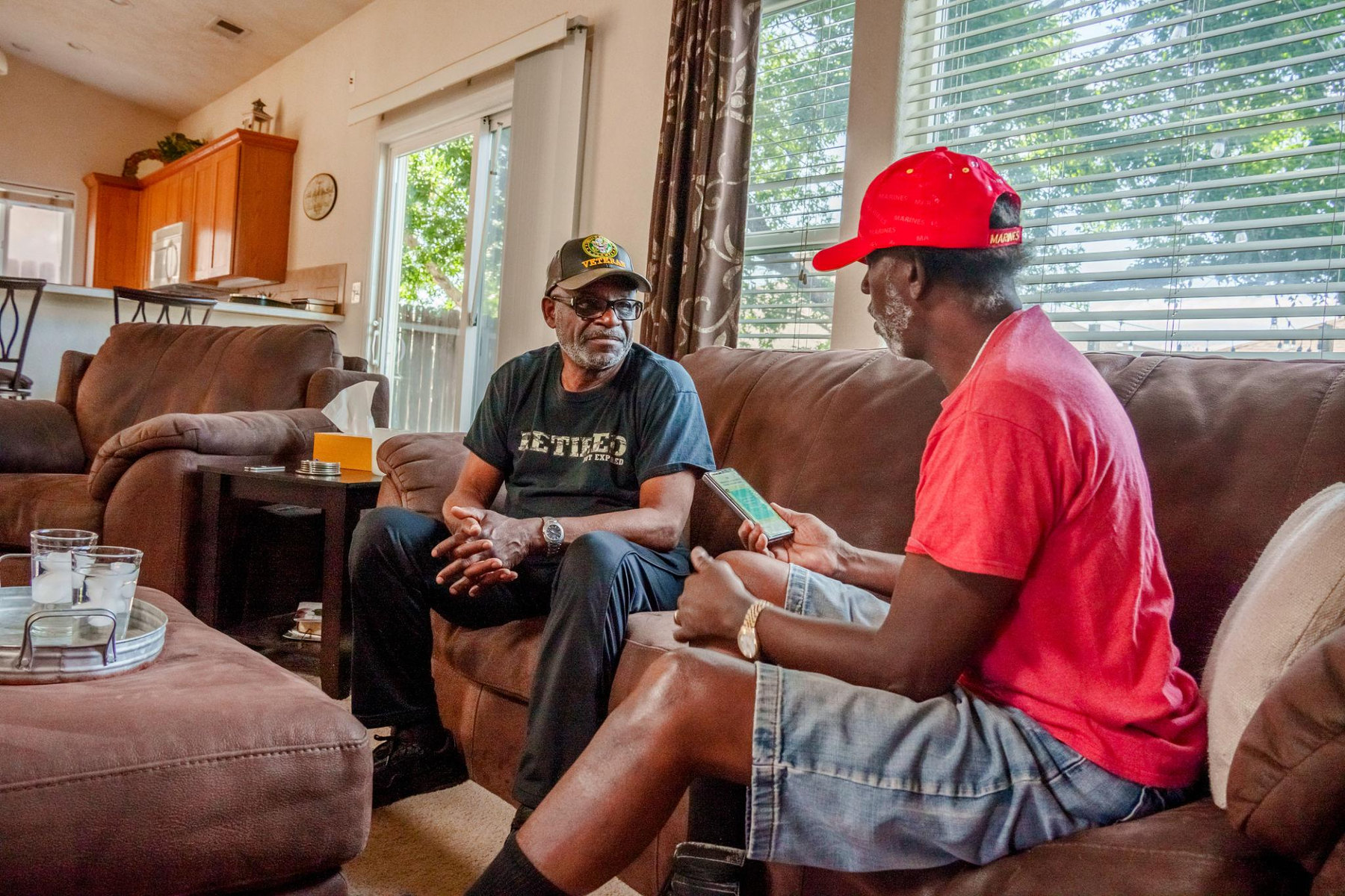 Two independent adult veterans talking inside a comfortable shared living room, one wearing a red shirt